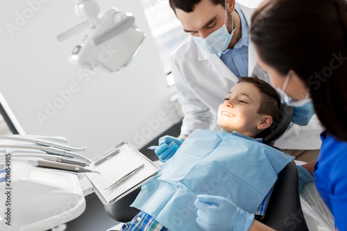 medicine  dentistry and healthcare concept - dentist with mouth mirror checking for kid patient teeth at dental clinic