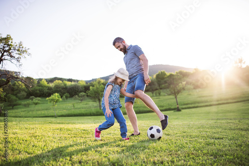 Father with a small daughter playing with a ball in spring nature.