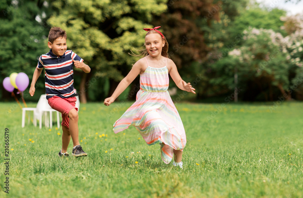 Naklejka premium friendship, childhood, leisure and people concept - happy kids or friends playing tag game at birthday party in summer park