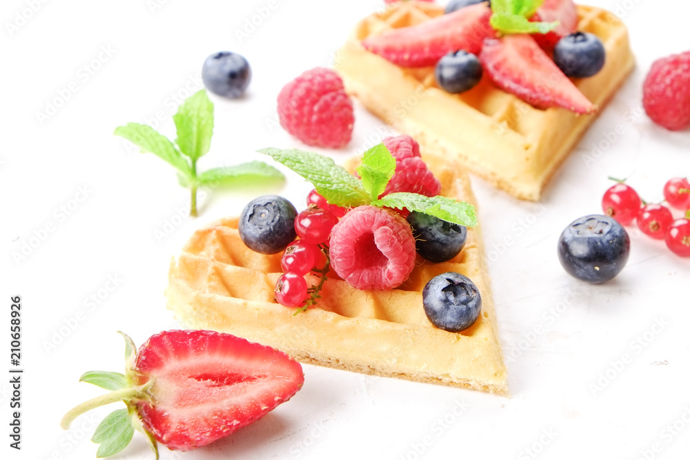 Heart shape belgium waffles with assorted berries mix, strawberry, blueberry, raspberry and red currant decorated with mint leaf on white ceramic plate. Close up, copy space, background, top view. Heart shape belgium waffles with assorted berries mix, strawberry, blueberry, raspberry and red currant decorated with mint leaf on white ceramic plate. Close up, copy space, background, top view.