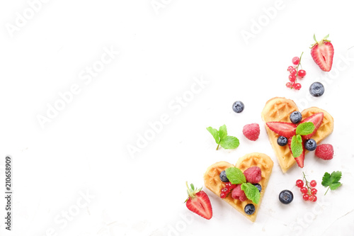 Heart shape belgium waffles with assorted berries mix, strawberry, blueberry, raspberry and red currant decorated with mint leaf on white ceramic plate. Close up, copy space, background, top view.