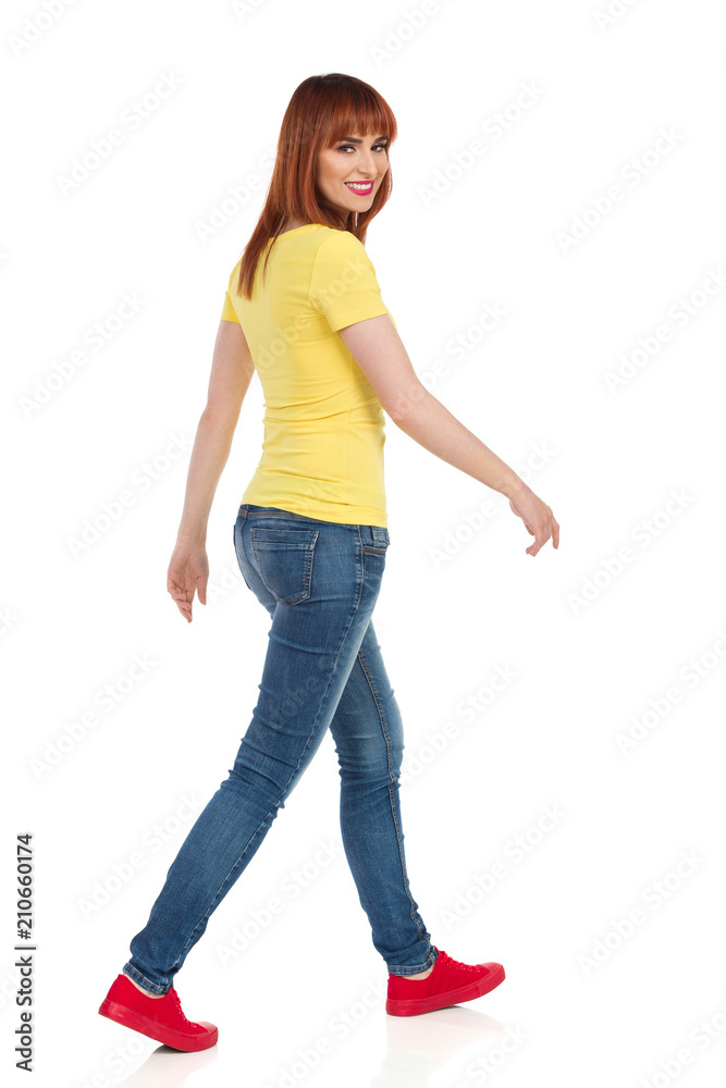 Young Casual Woman Is Walking And Looking At Camera Over The Shoulder Young Casual Woman Is Walking And Looking At Camera Over The Shoulder
