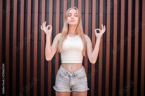 Light-haired girl is standing and meditating. She has her fingers in rounds. Girl is keeping her eyes closed. She is very calm and relaxed. Isolated on striped background. photo