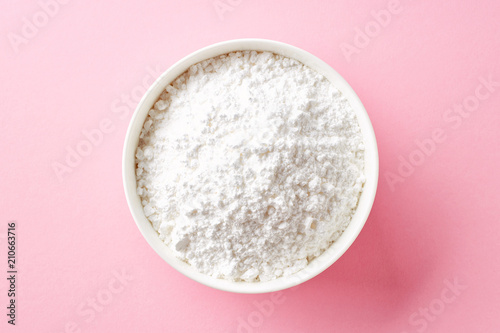 Bowl of powder sugar on white background, from above