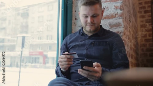 A young businessman who checks the balance on his account using an online banking application on his mobile phone.