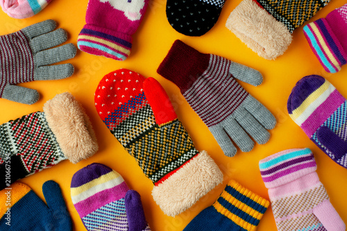 Warm clothes in the form of mittens and gloves. Colorful mittens and gloves scattered on a yellow background. View from above. photo