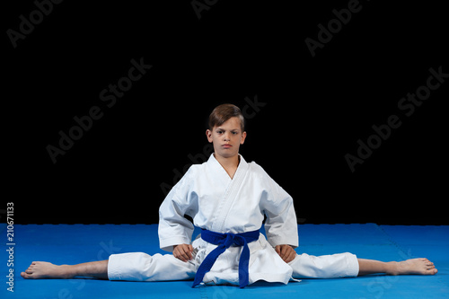 Karate kid wearing white gi and belt in a side split side straddle Chinese split, with arms crossed on