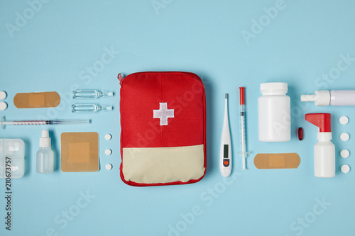 top view of red first aid kit bag on blue surface with medical supplies