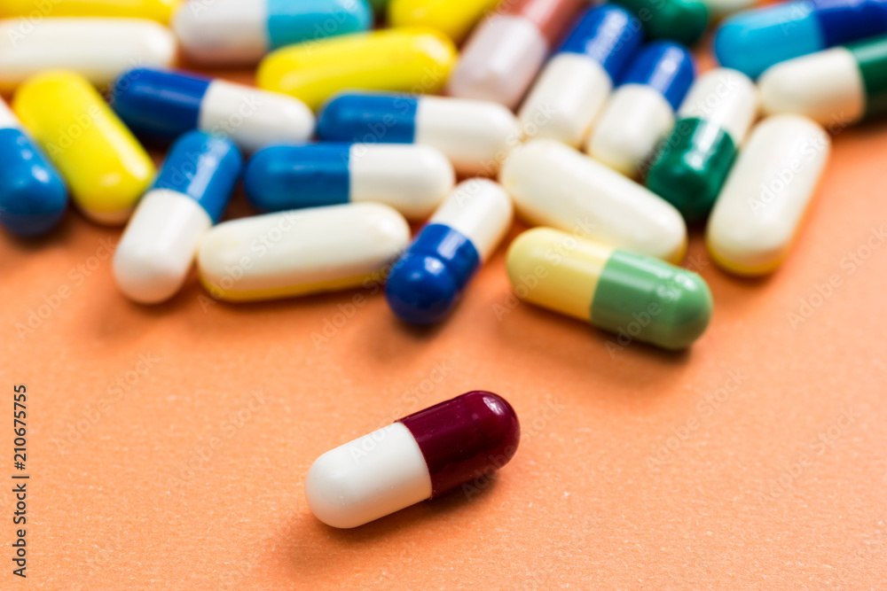Heap of assorted colorful capsules on orange background. One red and white pill is apart, isolated.