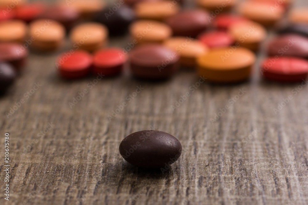 Heap of assorted orange, brown and red capsules on wooden table. Heap of assorted orange, brown and red capsules on wooden table.