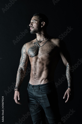 Tattooed man show sexy muscular torso. Sportsman with six pack and ab. Bodybuilder with biceps and triceps. Fashion model with tattoo in jeans. Bodycare with fitness and sport in vintage filter