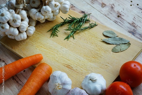 Many fresh ingredients, rosemary, spaghetti, carrot, tomato, garlic, onion and bay leaf on chopping board with wooden table background, cooking concept, copy space
