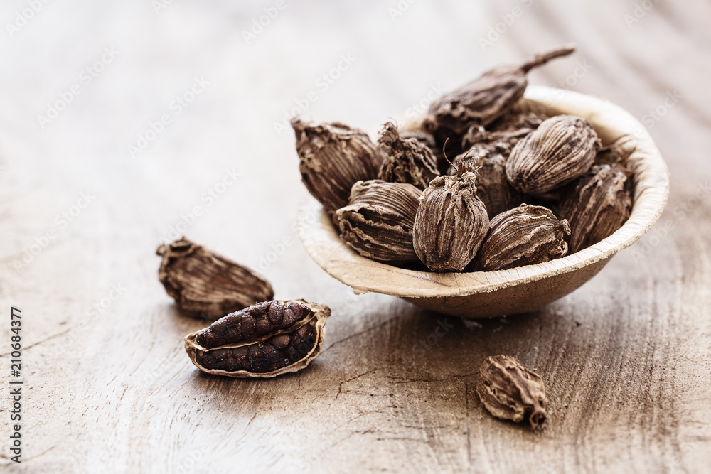Whole black cardamom in coconut bowl on wooden background close-up Whole black cardamom in coconut bowl on wooden background close-up