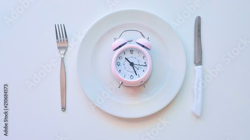 clock on an empty plate, white background. the concept of limiting the intake of food.