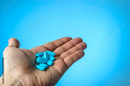 Blue pills in a patiens hands on blue background. Caring for the