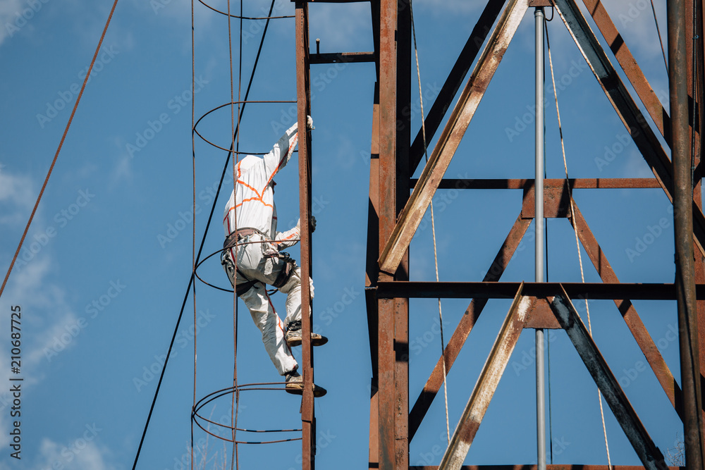 ndustrial climber in uniform and helmet climbing the stairs. Professional worker doing his risky job on water tower.