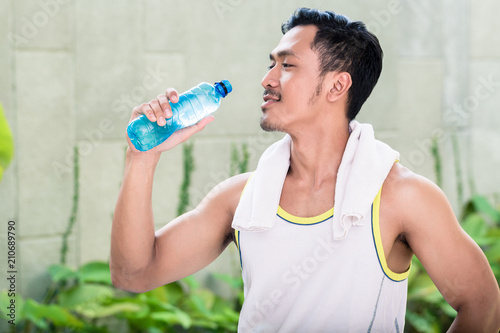 Asian man working out in his garden drinking water