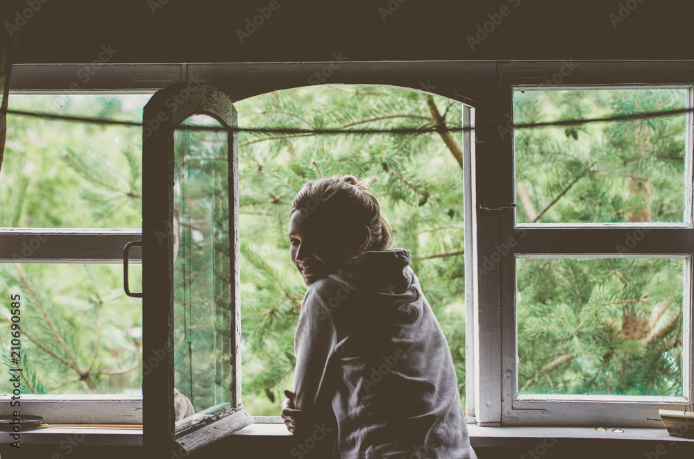 A woman standing by the window admires a view of nature in the A woman standing by the window admires a view of nature in the