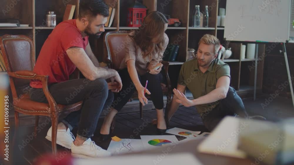 Creative business people discussion market graph on floor in cozy studio. Cheerful professional group discussing business strategy documents on floor. Creative business meeting. Creative brainstorm