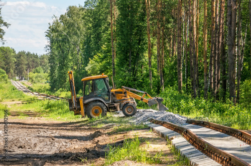 Yellow excavator pours gravel on the construction of the railway in the forest