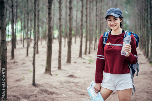 A young Asian female traveling with blue backpack waring a orange gap and looking a map in a pine forest somewhere in Thailand.
