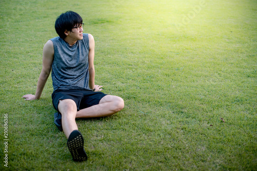 Young Asian man runner sitting on the grass after running
