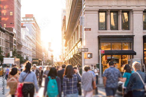 Diverse group of anonymous people walking down busy urban street with bright sunlight shining in the background in New York City