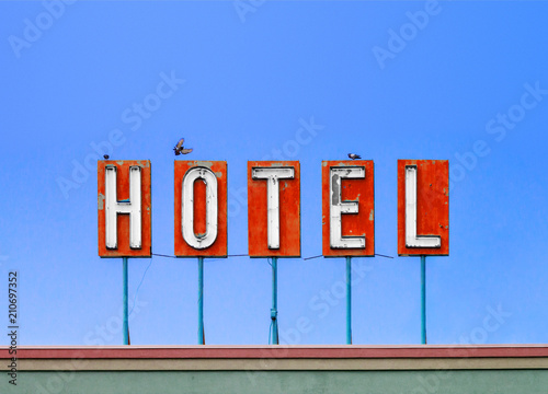 Red hotel sign on top of old motel isolated on blue sky background with birds photo