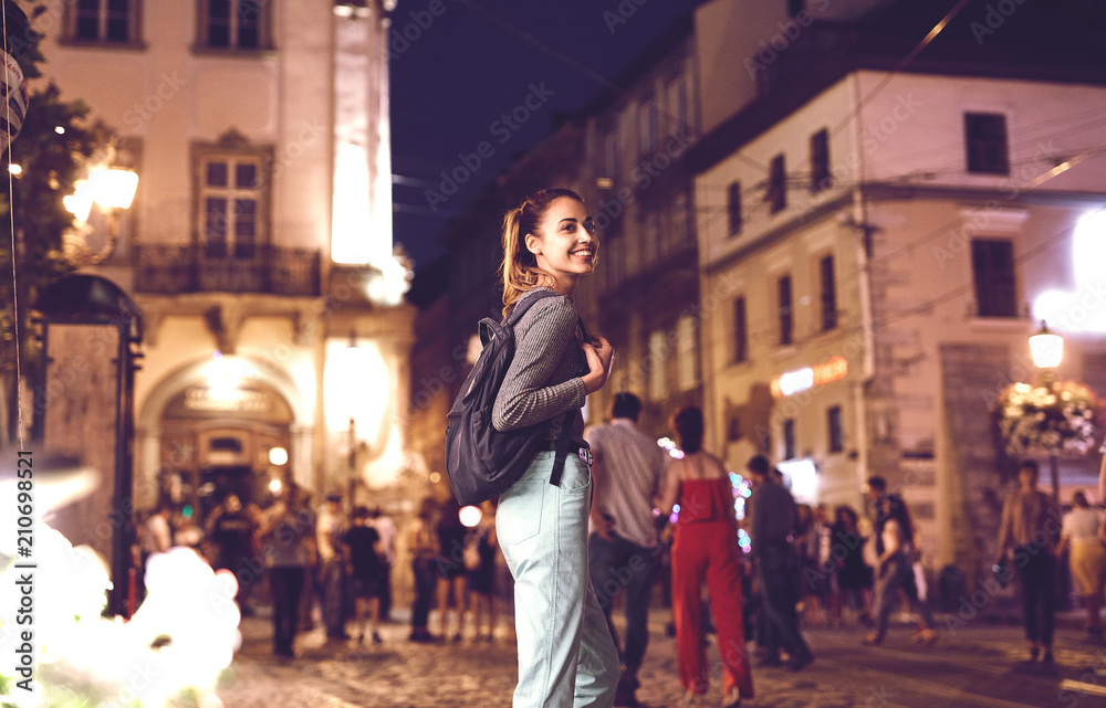 young woman tourist walking on the night street in historic part of city