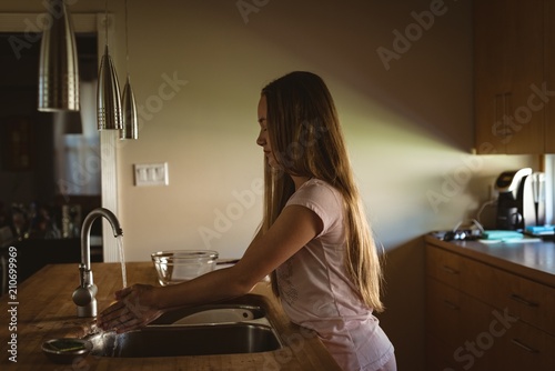 Girl standing in kitchen washing her hands under the tap water photo