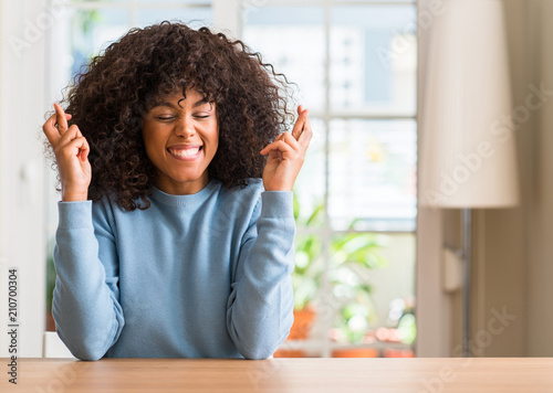 Fotografie African american woman at home smiling crossing fingers with hope and eyes closed