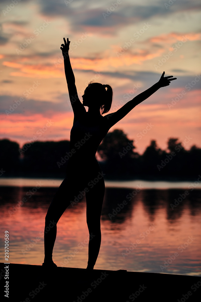 Sporty woman posing near city lake on sunset. Fitness, yoga, crossfit exercises. Fit, strong bodies, healthy lifestyle. Outdoors workout on fresh air. Colorful sky view. Water reflection.