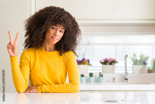 African american woman wearing yellow sweater at kitchen showing and pointing up with fingers number two while smiling confident and happy.
