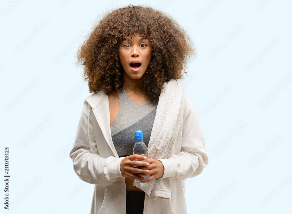 African american fitness woman holding water bottle scared in shock with a surprise face, afraid and excited with fear expression African american fitness woman holding water bottle scared in shock with a surprise face, afraid and excited with fear expression
