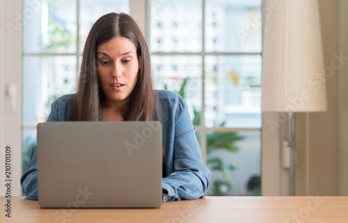 Young woman using laptop at home scared in shock with a surprise face, afraid and excited with fear expression