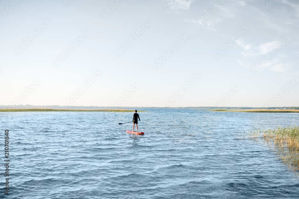 Man paddleboarding on the lake during the morning light, wide landscape view with blue water and sky Man paddleboarding on the lake during the morning light, wide landscape view with blue water and sky