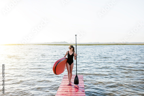 Beautiful woman standing on the pier with paddleboard and oar enjoying morning view on the lake © rh2010