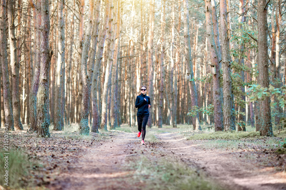 Woman in black sportswear running in the pine forest at the morning, wide landscape view