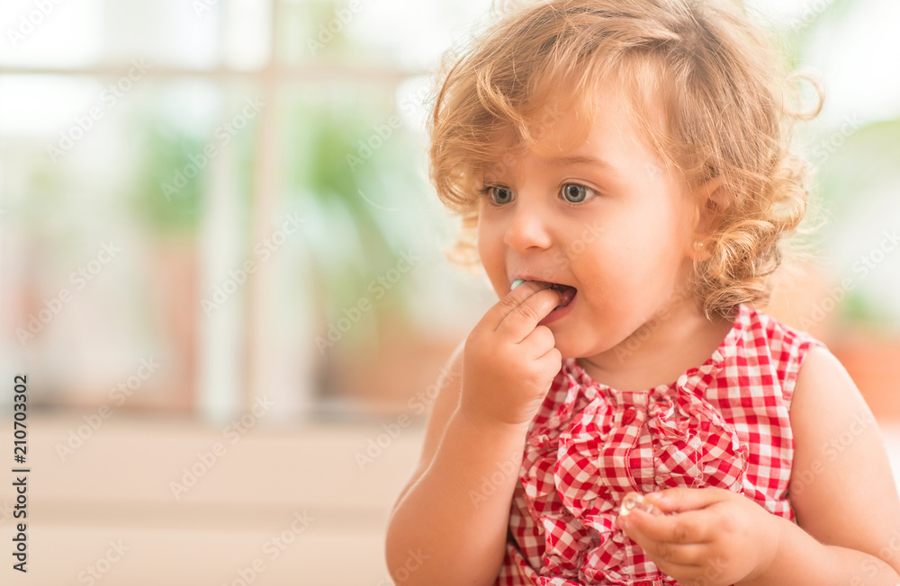 Beautiful blonde child with blue eyes eating candy at home. Beautiful blonde child with blue eyes eating candy at home.