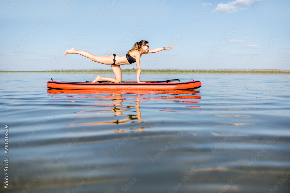 Young woman doing yoga on the paddleboard on the lake with calm water and reflection during the morning light