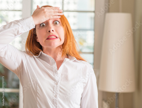 Redhead woman wearing white shirt at home stressed with hand on head, shocked with shame and surprise face, angry and frustrated. Fear and upset for mistake.