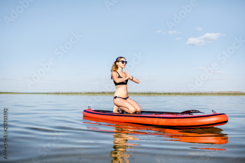 Young woman doing yoga on the paddleboard on the lake with calm water and reflection during the morning light © rh2010