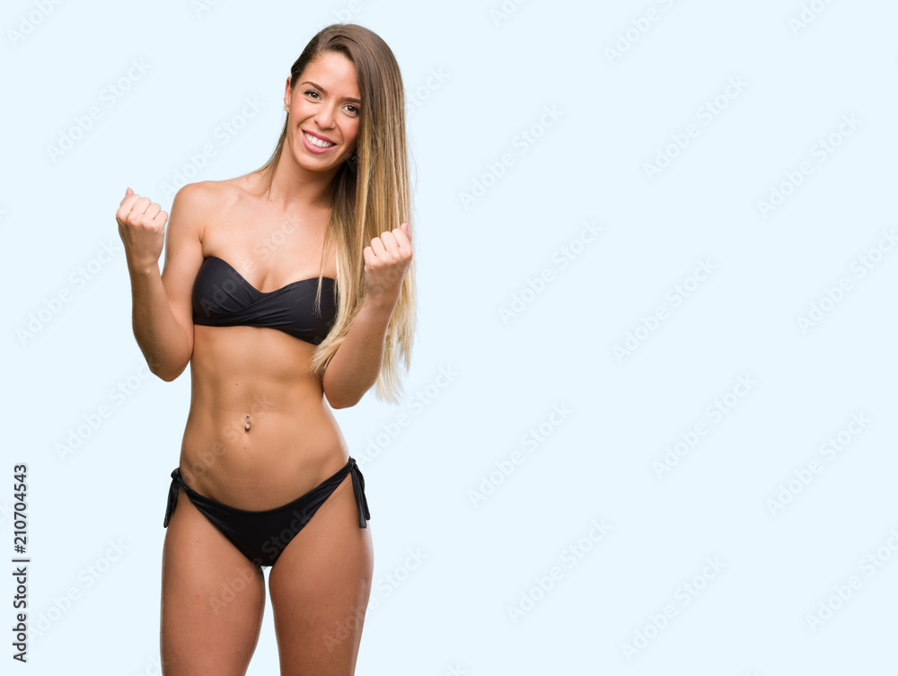Fototapeta premium Beautiful young woman wearing black bikini screaming proud and celebrating victory and success very excited, cheering emotion