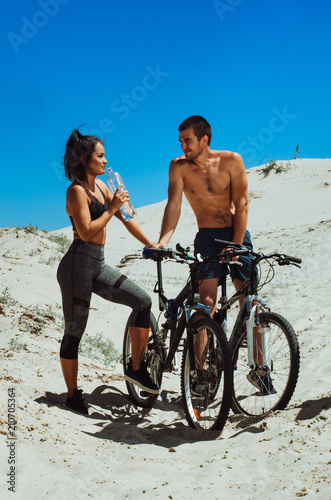 two athletes, a boy and a girl, play sports on the beach. guy black girl Asian . cyclists resting. drink water