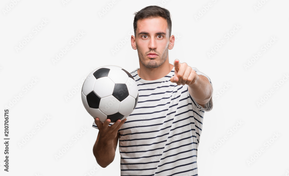 Handsome young man holding soccer football pointing with finger to the camera and to you, hand sign, positive and confident gesture from the front Handsome young man holding soccer football pointing with finger to the camera and to you, hand sign, positive and confident gesture from the front