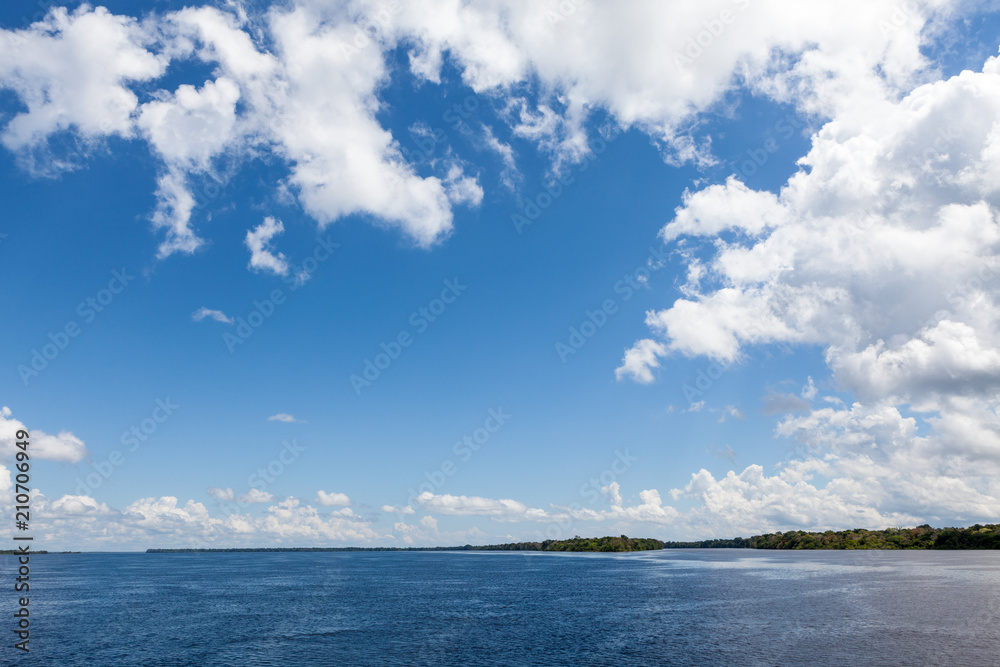 Amazonas, Brazil - River bank in the Amazon rainforest with dark waters of Negro river reflecting blue sky and clouds and forest in the background on a sunny day.