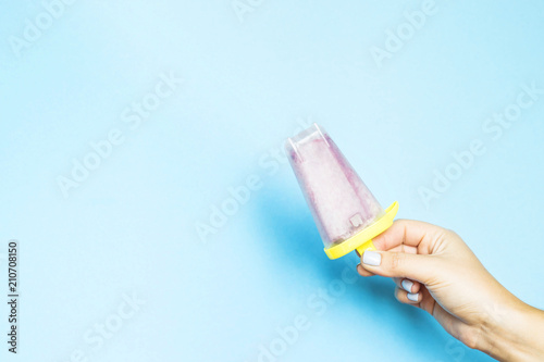 Berry homemade ice cream in plastic form in a female hand on a blue background. Summer healthy organic dessert