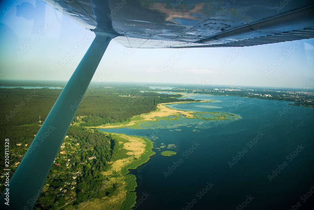 A beautiful aero landscape looking out of a small plane window under the wing. Riga, Latvia, Europe in summer. Authentic flying experience in a sunny, hazy day. Landscape from air. A beautiful aero landscape looking out of a small plane window under the wing. Riga, Latvia, Europe in summer. Authentic flying experience in a sunny, hazy day. Landscape from air.