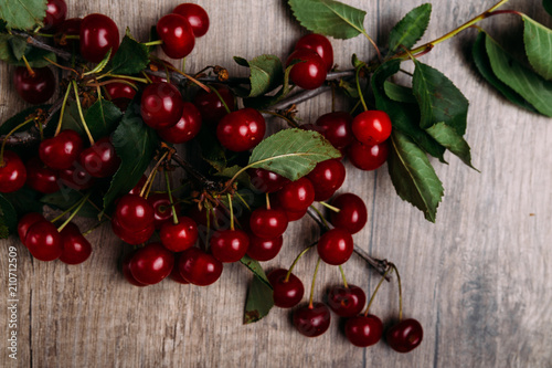 summer gifts. a fresh branch of a cherry tree with green leaves and red fruits, cherries lying on a wooden table, on a wooden background. Protect the environment. proper nutrition.place for text