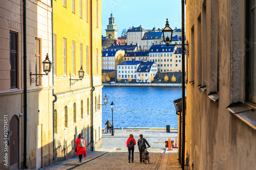 Tourists walking on cobble streets in Riddarholmen is part of Gamla stan is old town of Stockholm city, Sweden. Facades of medieval houses and exterior of historic buildings on shore of Baltic sea.